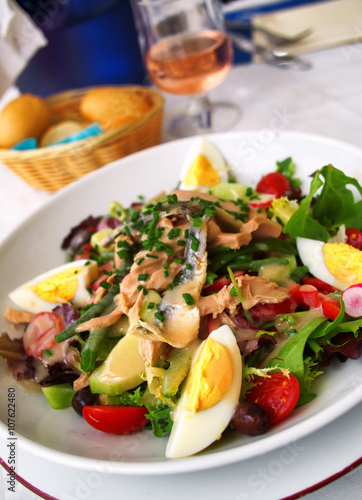 Nicoise Salad served in a restaurant in Cannes, France. Vertical shot, with bread and rose wine on background