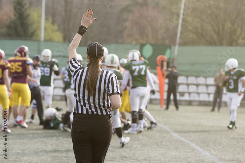 Female American football referee giving signals and blurred players in the background