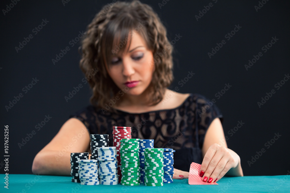 Young woman with a pile of gambling chips, looking her cards while playing texas holdem poker Young woman with a pile of gambling chips, looking her cards while playing texas holdem poker