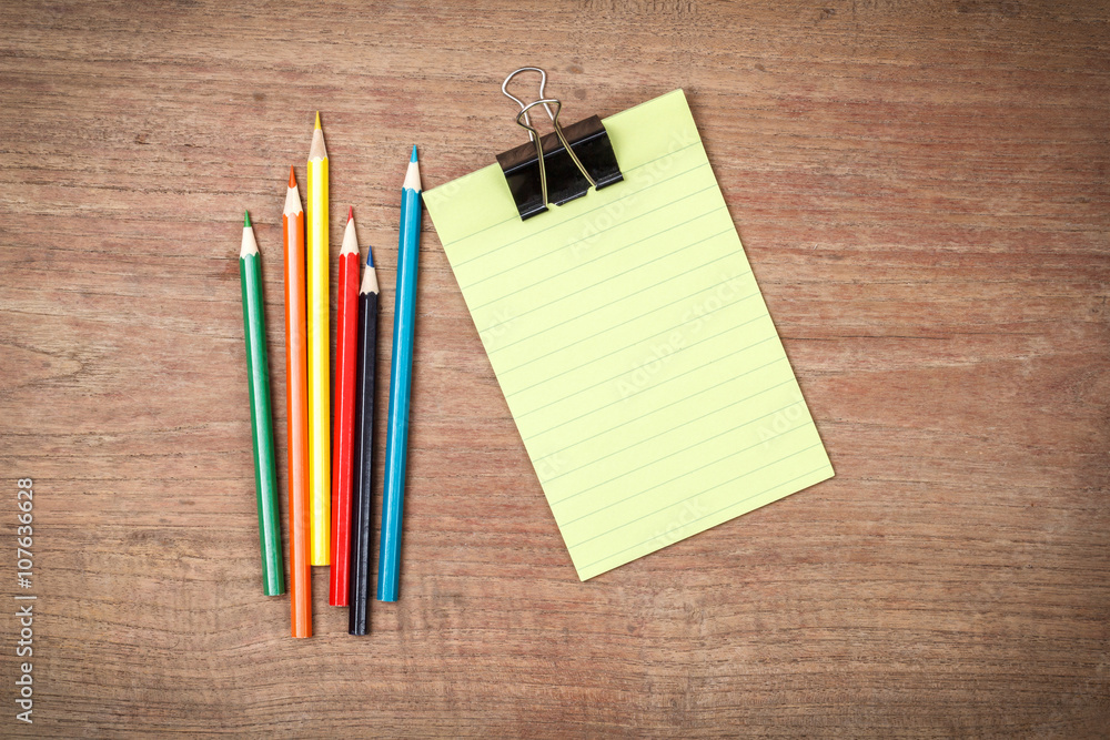 Green lined note paper with color pencils on wood table for back Green lined note paper with color pencils on wood table for back