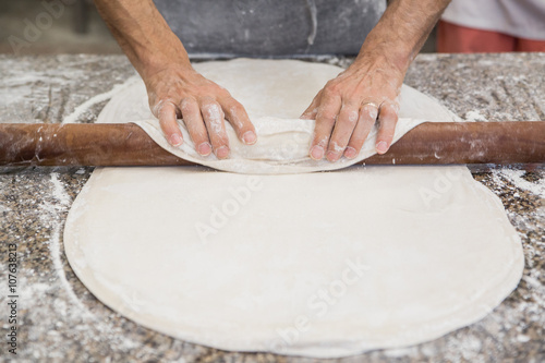 Hands baking dough with rolling pin on wooden table