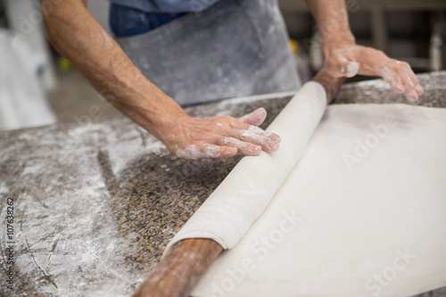 Hands baking dough with rolling pin on wooden table
