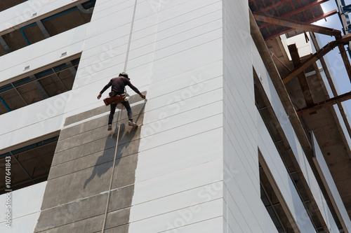 Worker painting high rise building in construction site.High risk working concept.