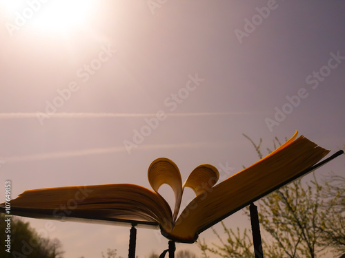 Stunning book in nature. Photo of a heart made from book pages photographed outdoor with beautiful sky in background.