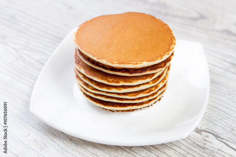 Tasty pancake on a white plate, wooden background, maple syrup Tasty pancake on a white plate, wooden background, maple syrup