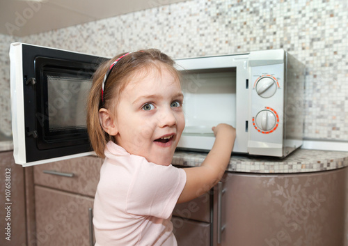 Fotografie Little girl playing with dangerous kitchen appliance