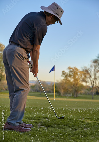 Man golfer chipping to putting green late afternoon golf round