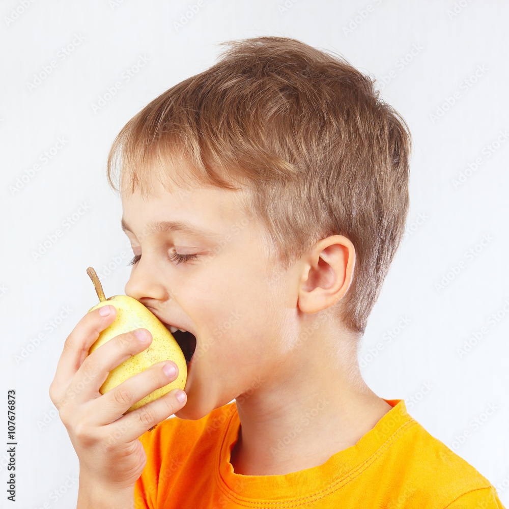 Little funny boy in a orange shirt eating a ripe yellow pear Little funny boy in a orange shirt eating a ripe yellow pear