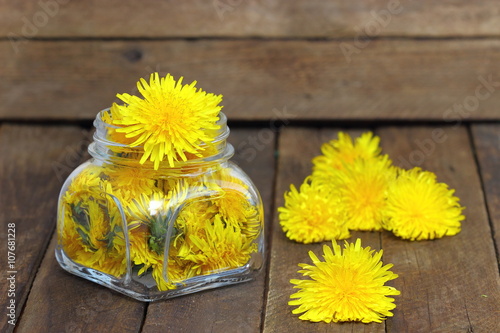 Flower honey in a glass jar and dandelions on a wooden table;