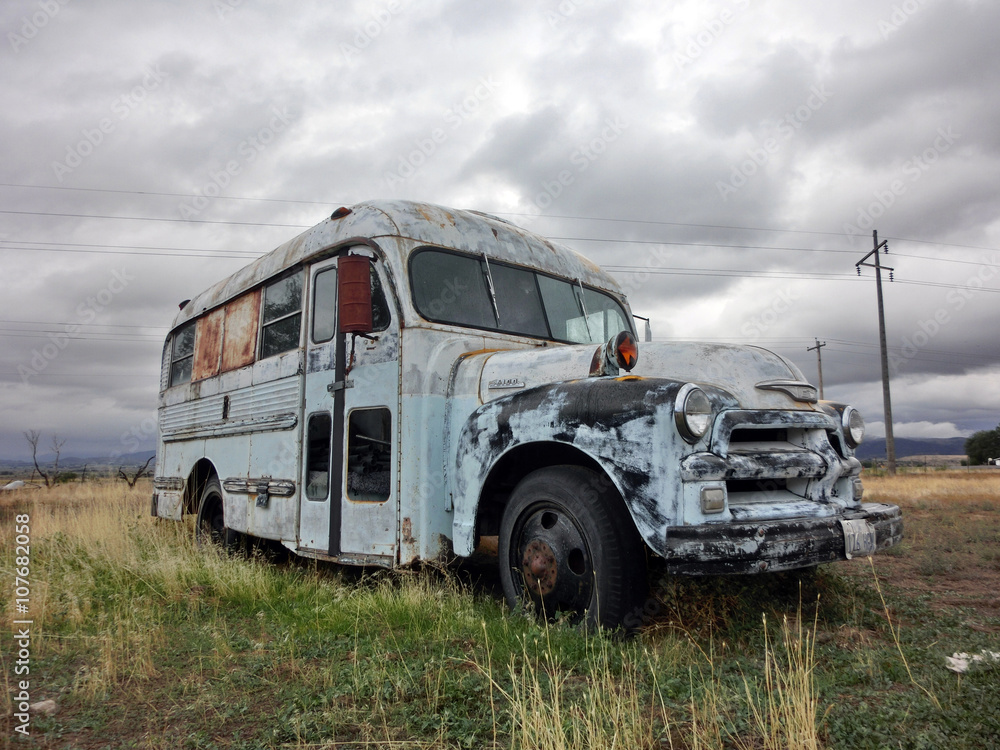 Abandoned rusty white metal bus in overgrown field - landscape color photo