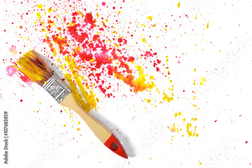 Paint brush with red and yellow gouache sprays near on white canvas in top view