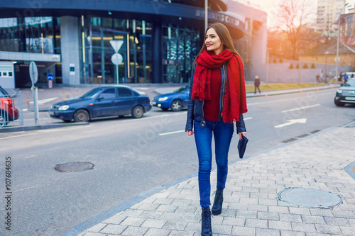 Fashion shot of pretty young woman over city background, wearing red scarf. City lifestyle. Female fashion