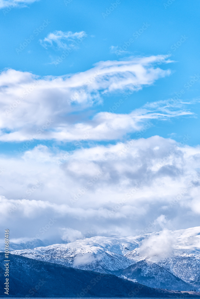 Snow caped mountain range under a blue cloudy sky. Vertical composition