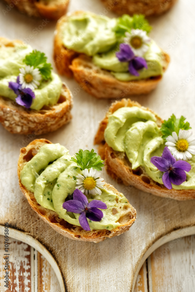Sandwiches with avocado paste with the addition of edible flowers violets and daisies