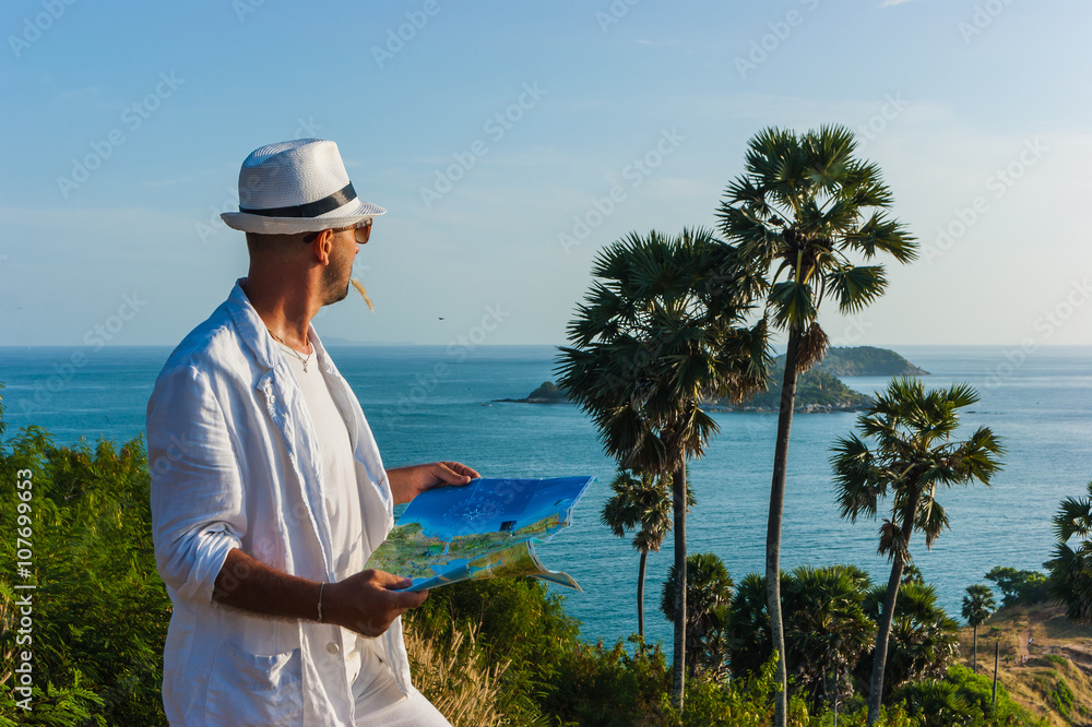 The man  in a white suit and hat sitting on a rock on the sea ba