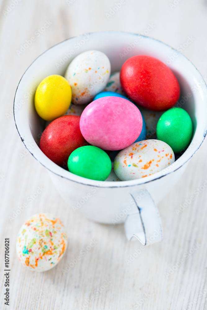 Easter candy eggs in miniature cup on wooden surface Easter candy eggs in miniature cup on wooden surface