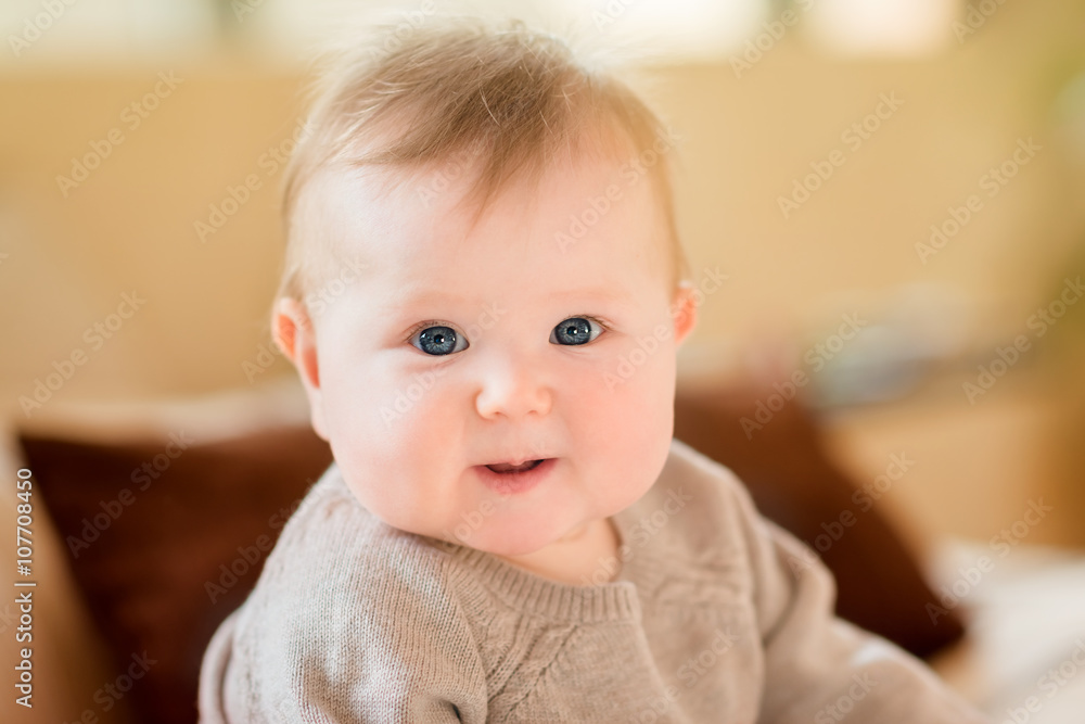 Closeup portrait of smiling little child with blond hair and blue eyes wearing knitted sweater sitting on sofa and looking at camera. Happy childhood