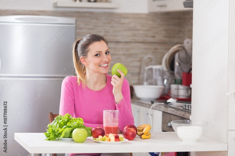 Healthy cheerful woman eating and apple an sitting in kitchen. Healthy cheerful woman eating and apple an sitting in kitchen.