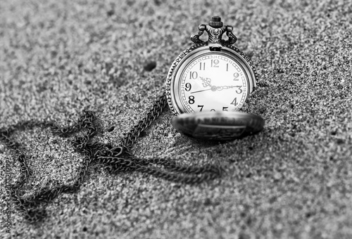 Vintage pocket watch is on the sand. Old metal watch with chain is on the sandy beach. 