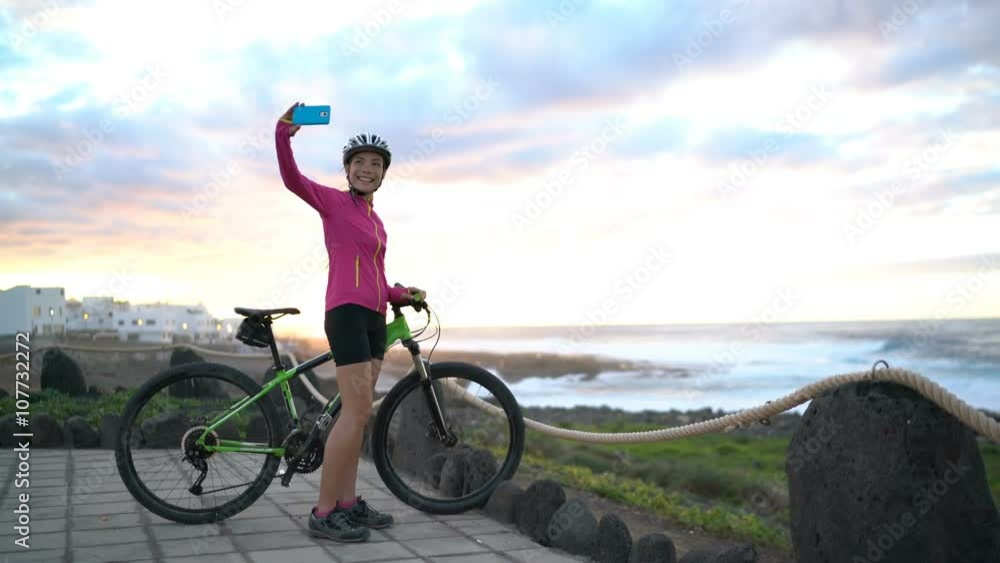 Mountain biking MTB cyclist woman cycling on bike relaxing taking selfie with smart phone at sunset view. Female mountain biker enjoying healthy active lifestyle on Lanzarote, Canary Islands, Spain Mountain biking MTB cyclist woman cycling on bike relaxing taking selfie with smart phone at sunset view. Female mountain biker enjoying healthy active lifestyle on Lanzarote, Canary Islands, Spain