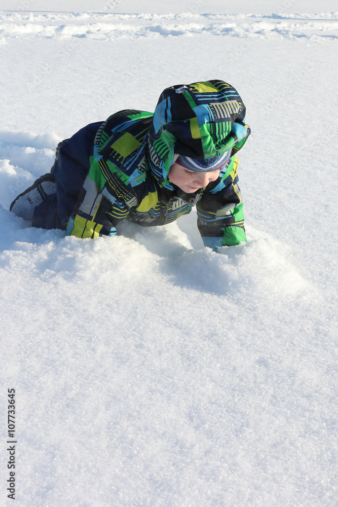 The little boy in a color jacket creeping on snow in the winter The little boy in a color jacket creeping on snow in the winter