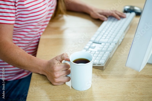 female hands holding a coffee cup and typing