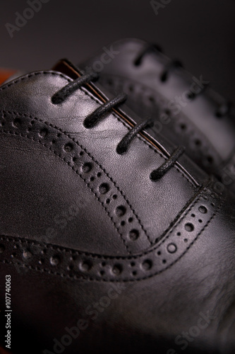 black oxford shoes with shoelace on black background closeup, top view