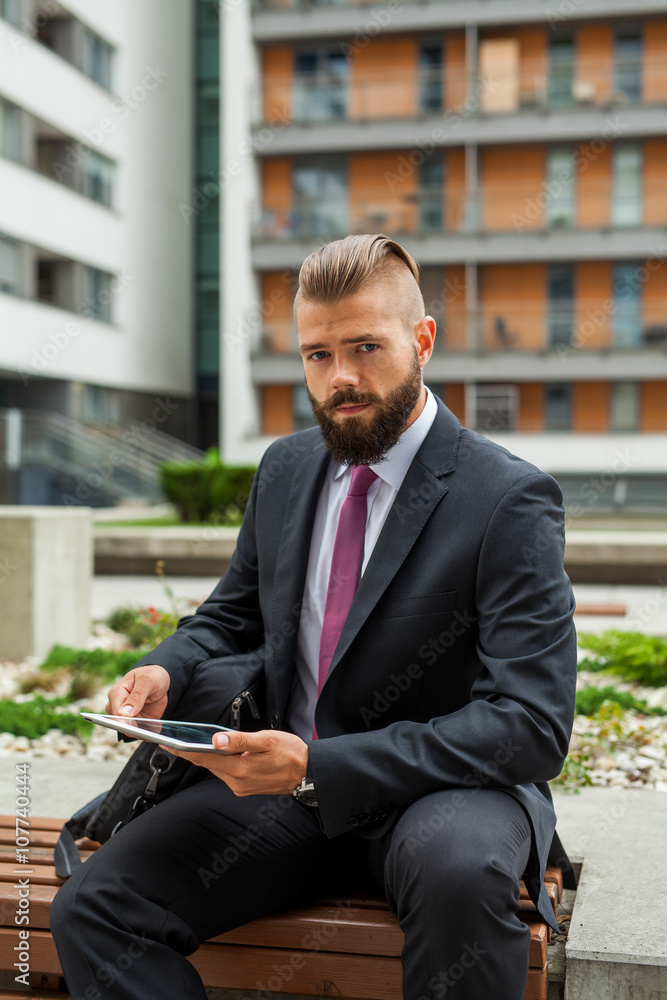 Young bearded businessman sitting on a bench and using tablet pc Young bearded businessman sitting on a bench and using tablet pc