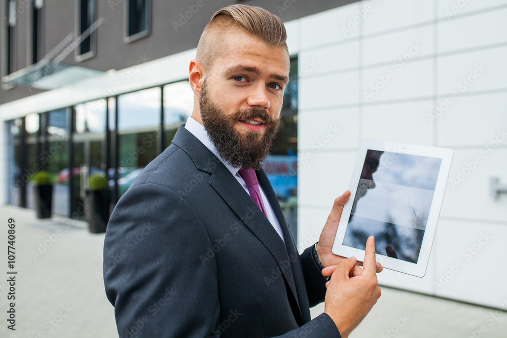 Fototapeta premium Young bearded businessman showing charts on tablet pc. Outdoor p