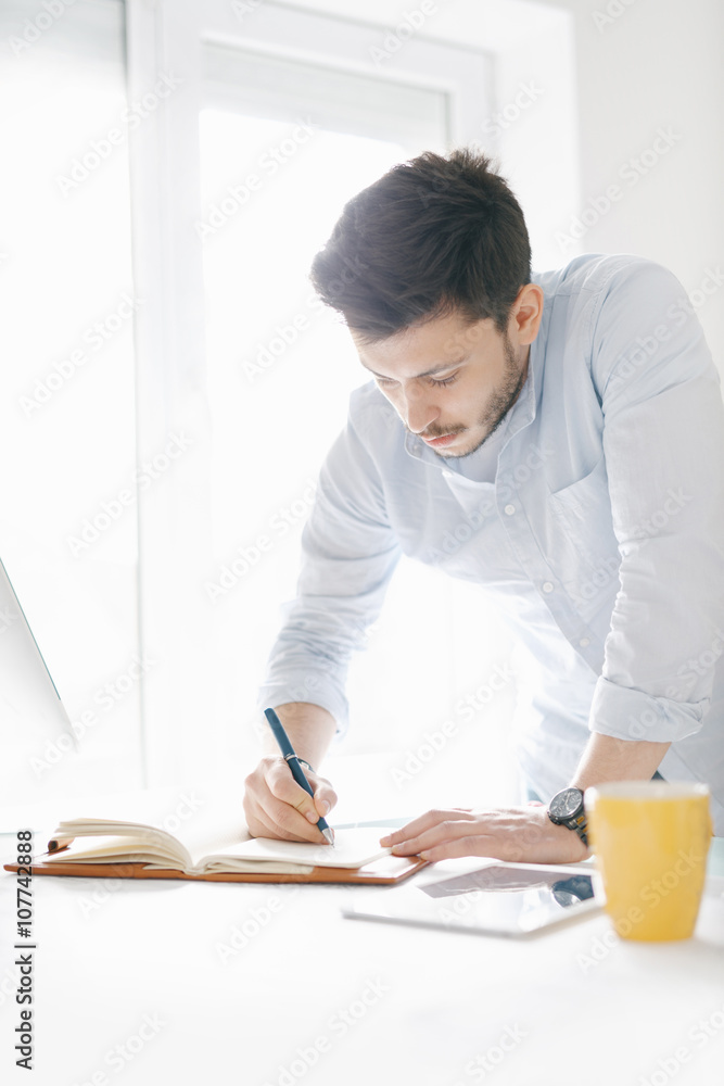 Young man in a modern office design sketching construction project design in a note book computer and drinks coffee Young man in a modern office design sketching construction project design in a note book computer and drinks coffee
