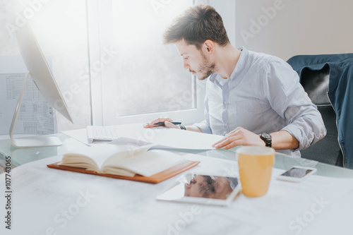 Young man in a modern office design sketching construction project design in a note book computer and drinks coffee