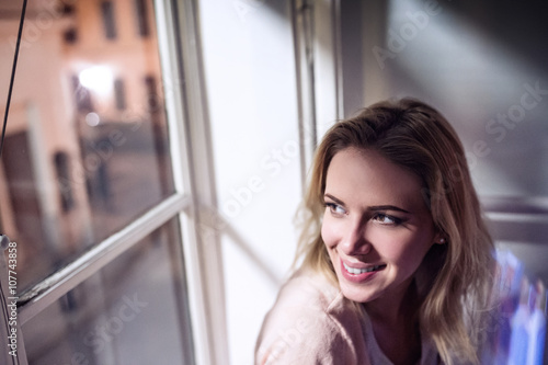 Woman sitting on windowsill, looking out of window, smiling