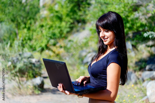 smiling brunette girl using laptop on a green grass background.