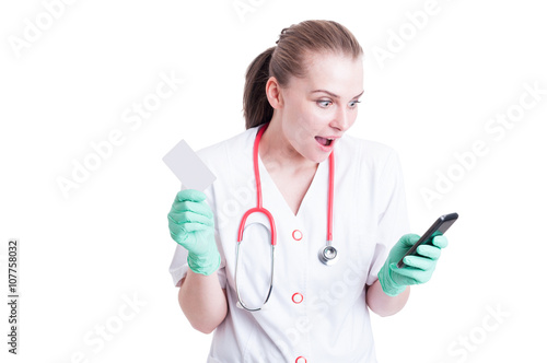 Surprised young doctor with cellphone and business or visit card