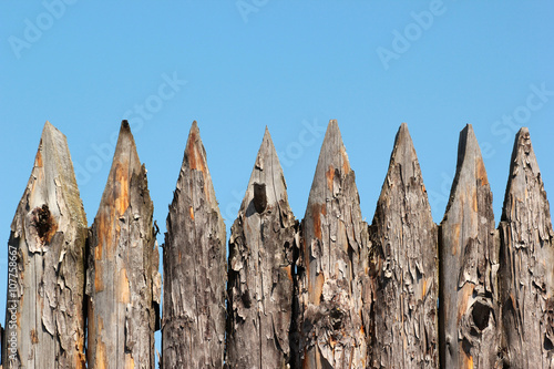 Photos Stockade wooden fence on blue sky background