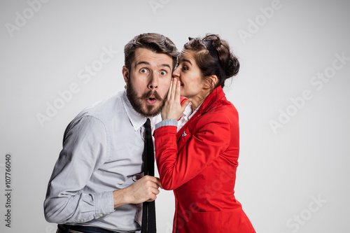 Young man telling gossips to his woman colleague at the office