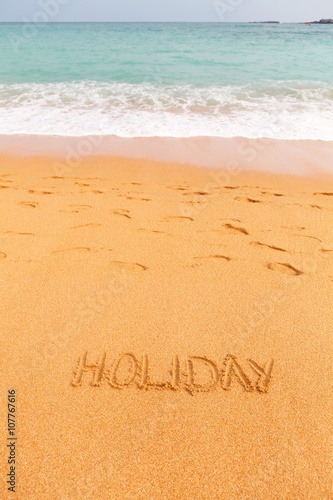 Inscription "Holiday" made on the beach by the blue sea
