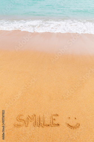 Inscription "SMILE :)" made on the beach by the blue sea