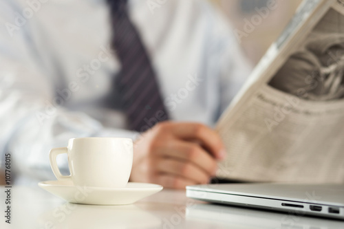 Cup of coffee with businessman reading newspaper on background