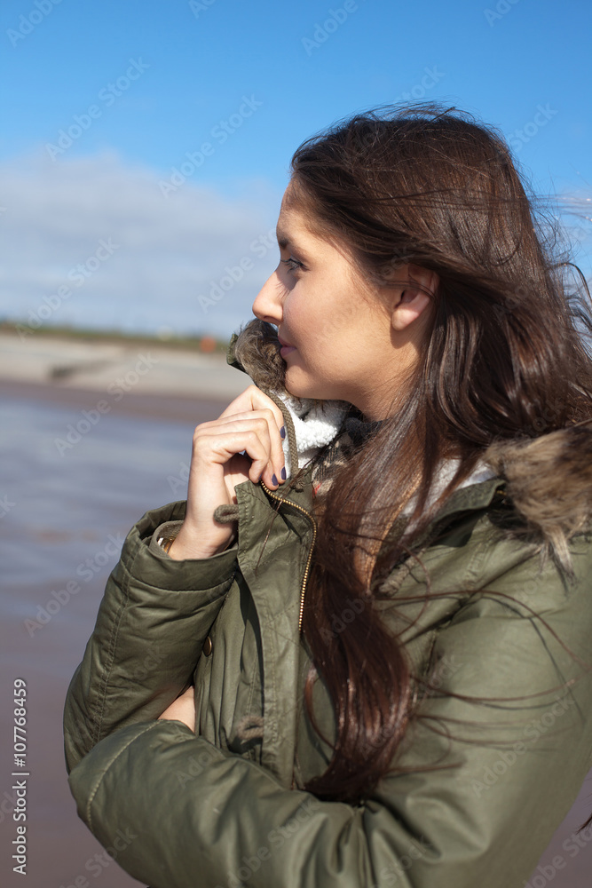Beautiful young woman huddling in her coat on a windy day at the Beautiful young woman huddling in her coat on a windy day at the