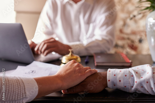 Multi ethnic couple hold hands at hotel check in desk, detail