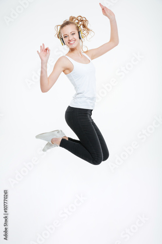 Fototapeta Naklejka Na Ścianę i Meble -  Cheerful young woman listening to music with headphones and jumping