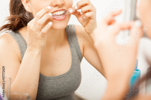 Tablou pe pânză Closeup of a woman putting a whitening strip on her teeth