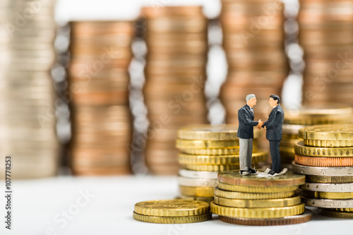 Businessman shake hands business on stack of money coin.