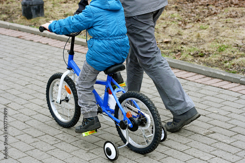 A boy with his father learning to ride a bike.