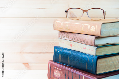 Stack of books with glasses on wooden desk  