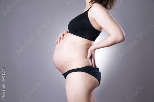 Caucasian pregnant woman in black lingerie with back pain on gray studio background