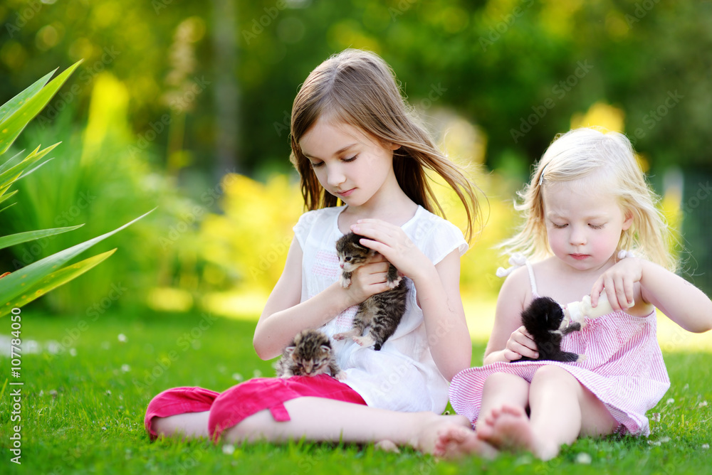 Two adorable little girls feeding small kittens with kitten milk from the bottle Two adorable little girls feeding small kittens with kitten milk from the bottle