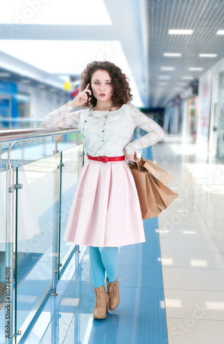 Caucasian girl in the mall shopping and talking on the phone. Portrait of a girl with shopping bags on the background of shop window. Happy shopper.