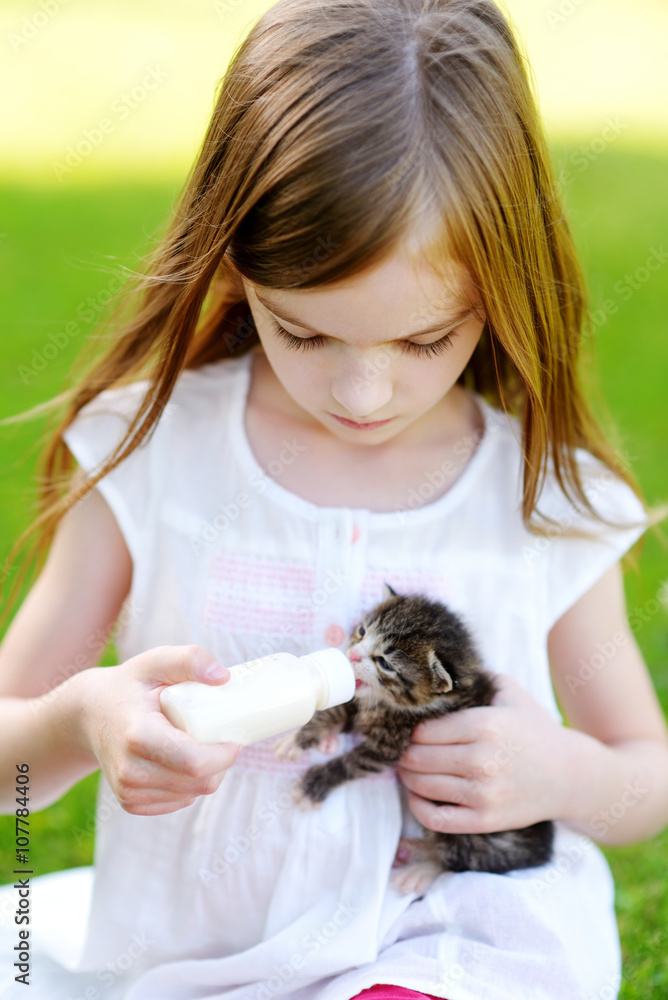 Adorable little girl feeding small kitten with kitten milk from the bottle Adorable little girl feeding small kitten with kitten milk from the bottle